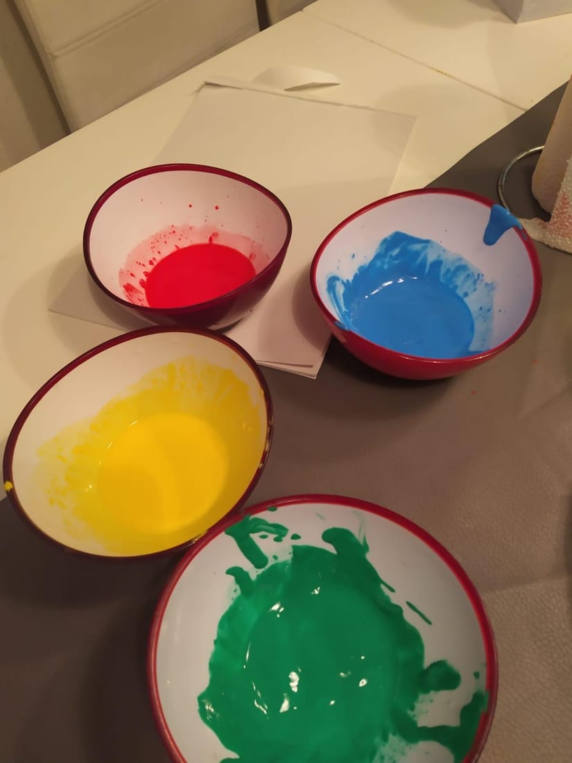 Vier Schälchen mit roter, blauer, gelber und grüner Fingerfarbe auf dem Tisch