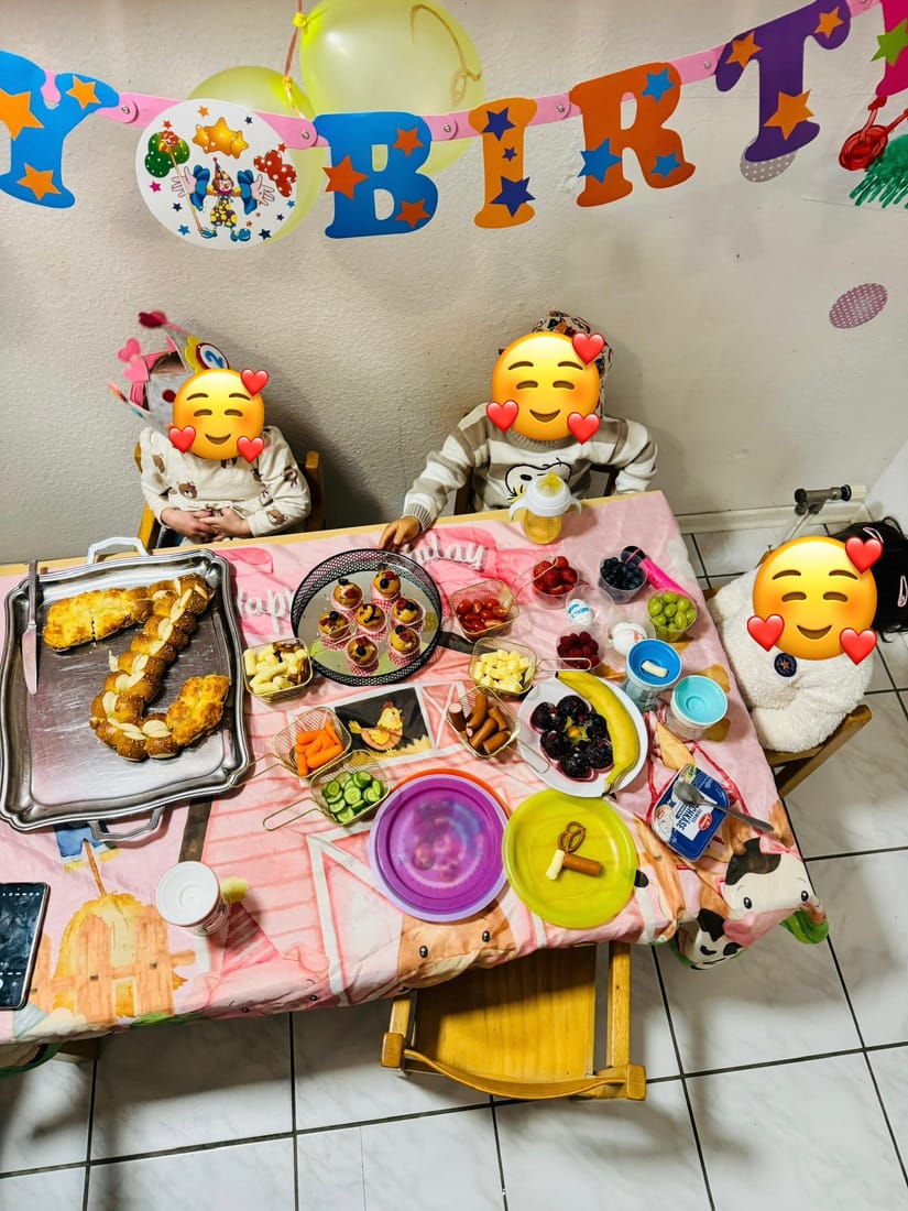 Festlich gedeckter Geburtstagstisch mit Brezel-Zahl, Muffins und Obst, dahinter feiernde Kinder