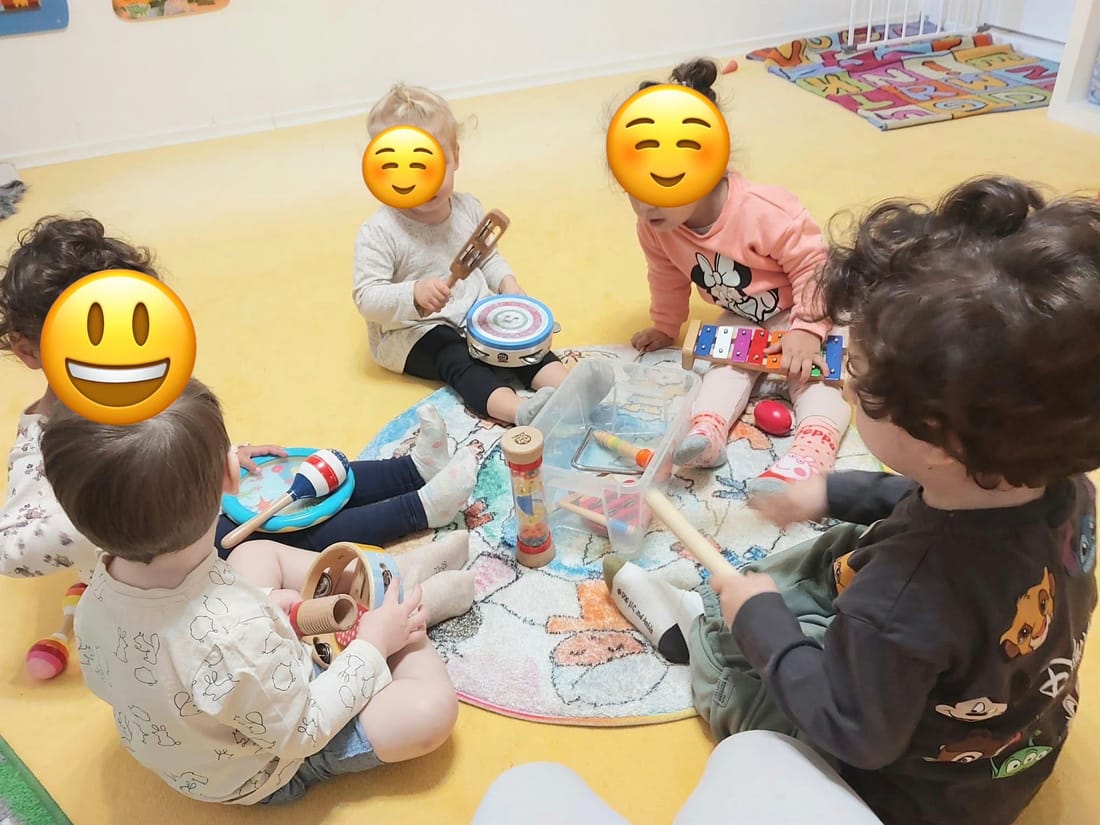 Kinder sitzen im Kreis auf dem Teppich und musizieren mit Tamburin, Xylophon und Rasseln