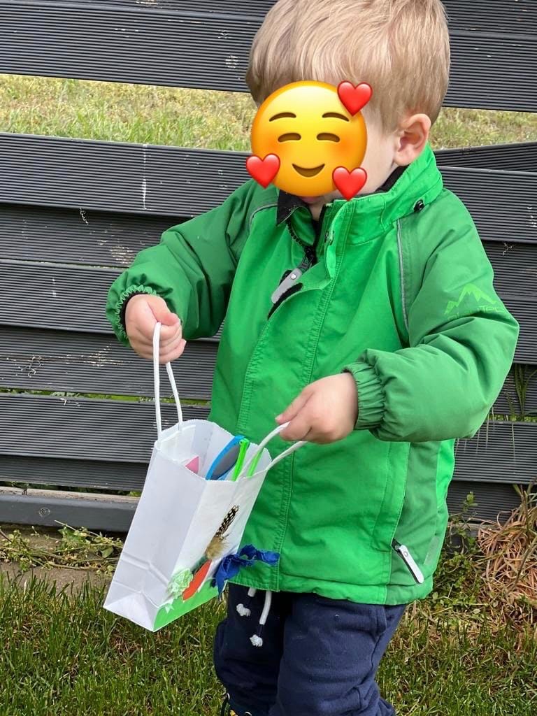 Ein Kind sammelt mit einer selbst gebastelten Tüte Gräser und Blätter am Zaun