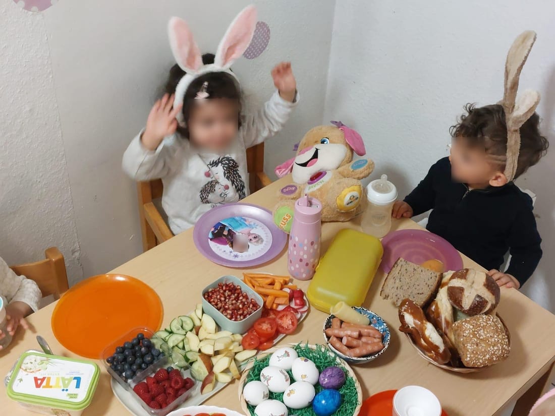 Österlich gedeckter Frühstückstisch mit bemalten Eiern, Obst und Gemüse, zwei Kinder mit Hasenohren