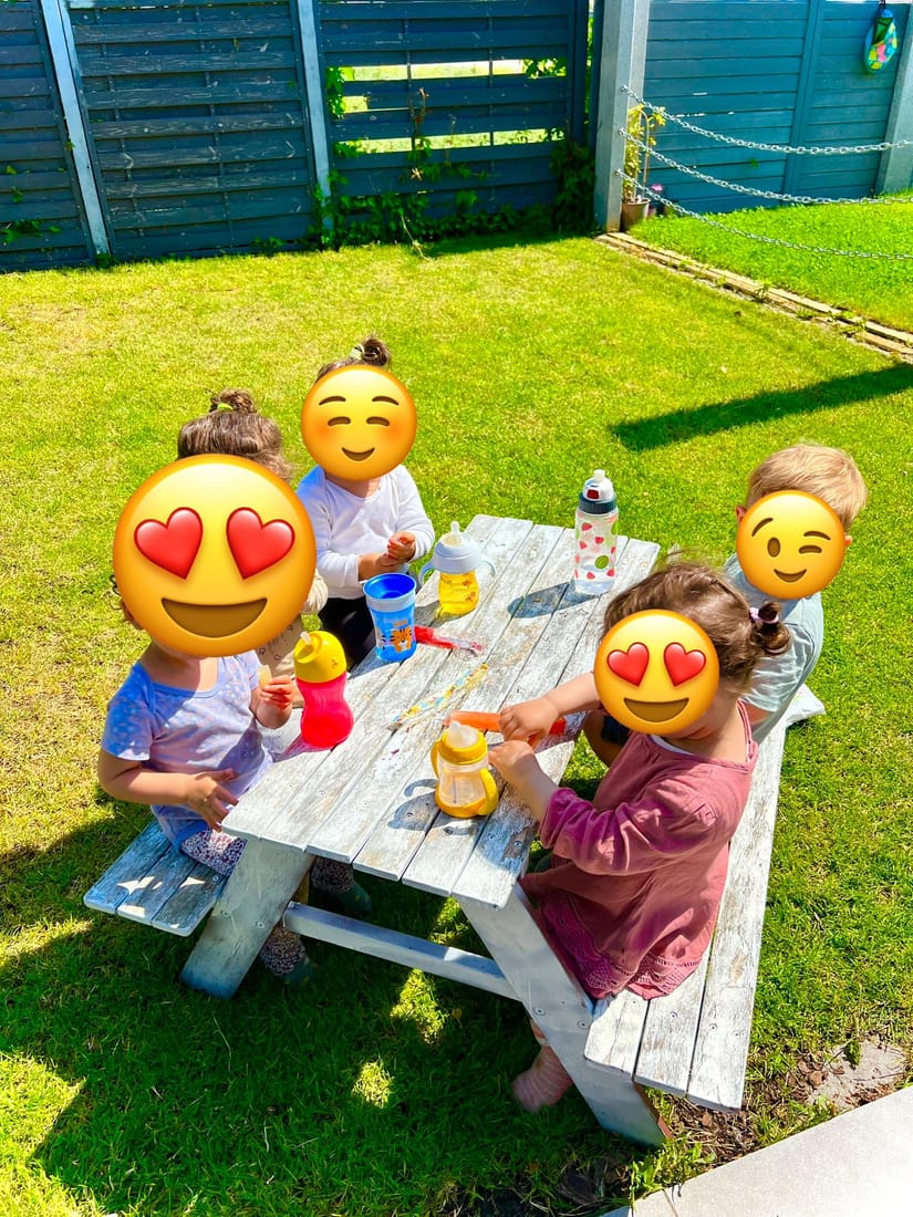 Vier Kinder sitzen an der Kinder-Picknickbank im Garten und trinken aus ihren Flaschen