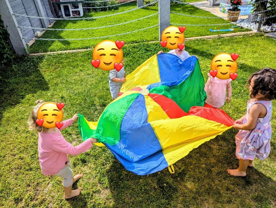 Fünf Kinder halten gemeinsam ein buntes Schwungtuch auf der Wiese