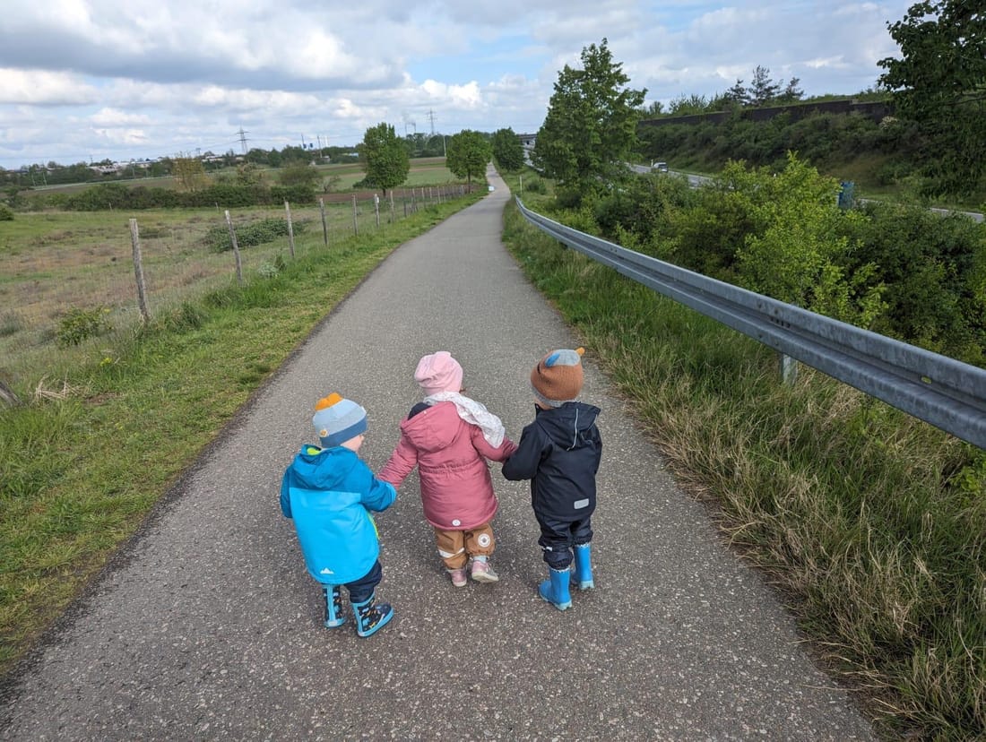 Drei Kinder gehen Hand in Hand einen Feldweg entlang