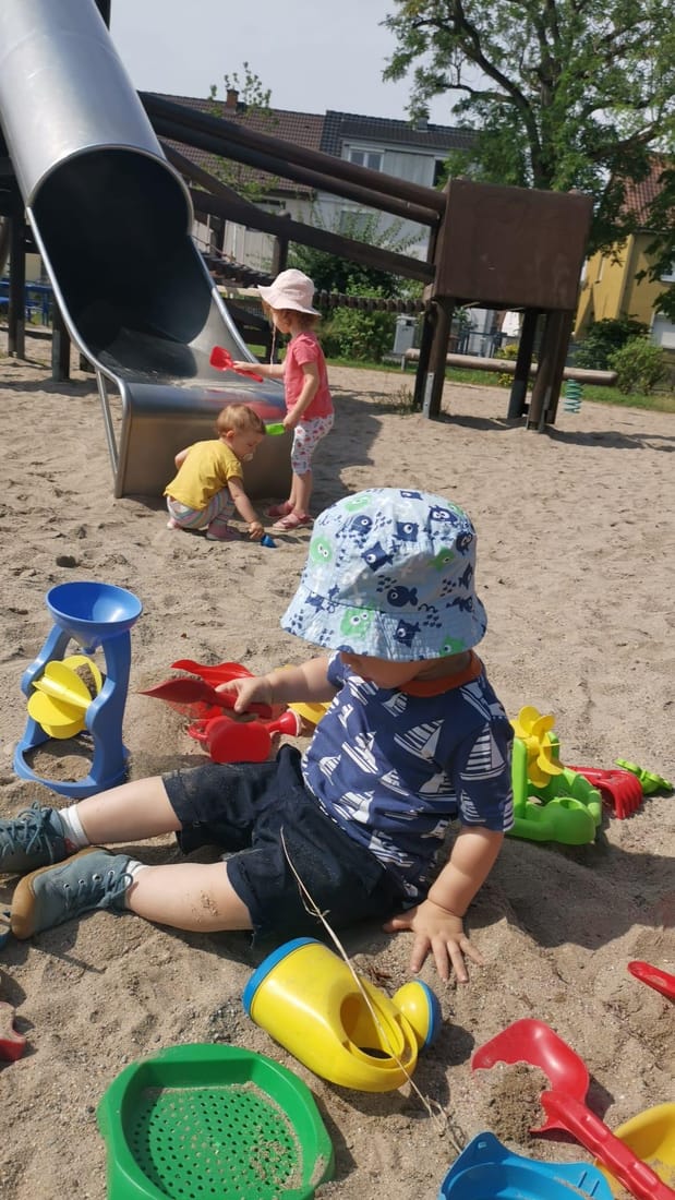 Kinder spielen mit Eimern und Schaufeln im Sand vor der großen Rutsche