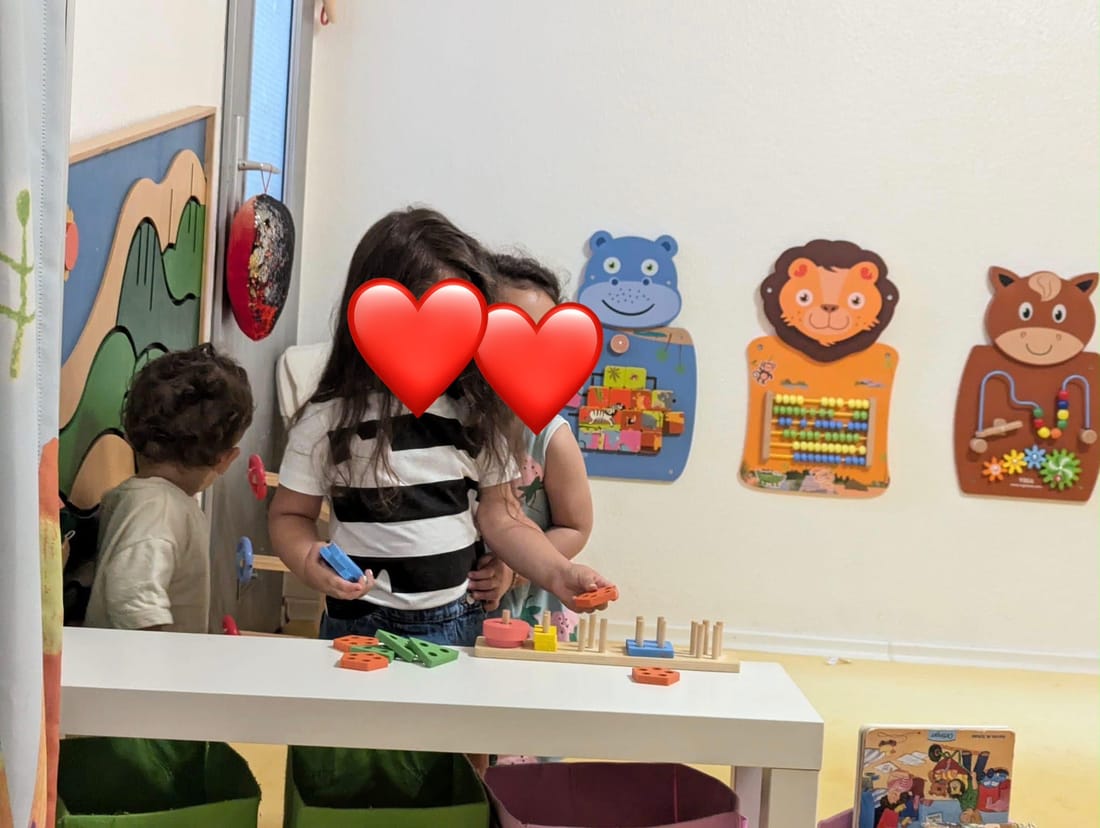 Kinder spielen zusammen an einem Tisch mit bunten Steckspielen, an der Wand hängen Motorik-Tafeln