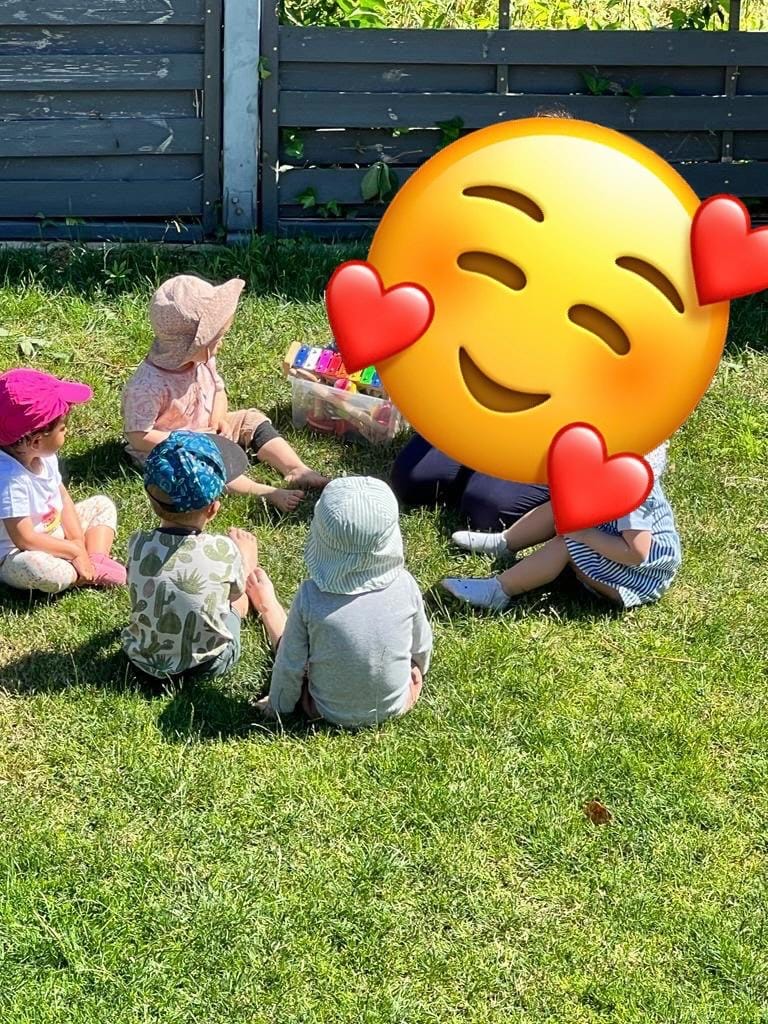 Kinder sitzen im Kreis auf dem Rasen um eine Kiste mit Instrumenten